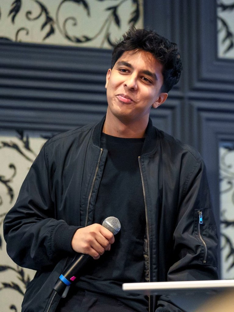 Rishi smiling while holding a microphone at an event